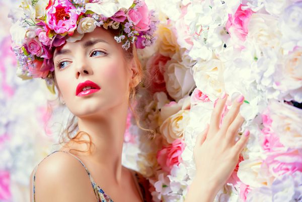 زن جوان عاشقانه زیبا در تاج گلی که روی پس زمینه گل رز ژست گرفته است الهام بخش بهار و تابستان مفهوم عطر لوازم آرایشی