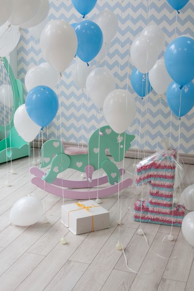 کودک یک ساله است اتاق کودک روشن با بادکنک تزئین شده با یک کیک هدیه یک اسب اسباب بازی و یک عدد بزرگ کاغذ رنگی