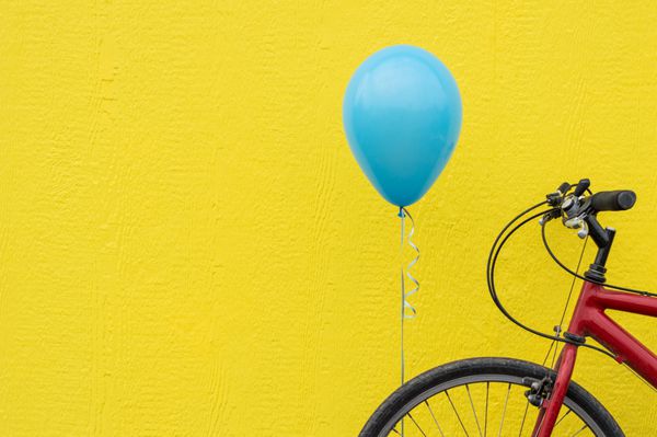 دوچرخه قرمز با یک بالون آبی در برابر دیوار زرد روشن
