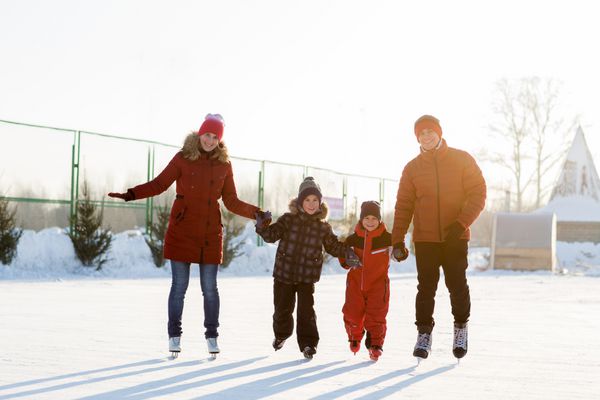 خانواده جوان شاد در زمستان در زمین بازی اسکیت می کنند خانواده ای زیبا که در زمستان روی یخ راه می روند و بازی می کنند