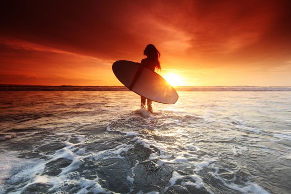 زن موج سوار در ساحل در غروب آفتاب