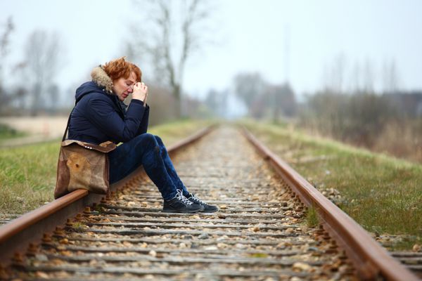 زن افسرده ای که روی ریل قطار نشسته و راهی برای خروج نمی بیند