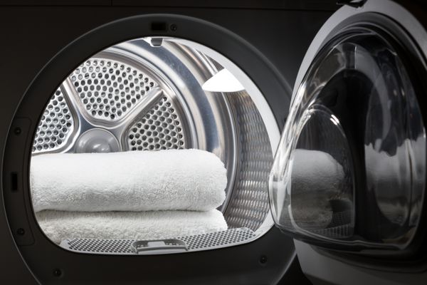 انباشته حوله های سفید تمیز در داخل درام ماشین لباسشویی مفهوم تمیز خشکشویی نمای نزدیک از ماشین لباسشویی باز