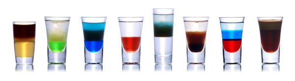 مجموعه ای از کوکتل های الکلی رنگارنگ در لیوان های شات جدا شده روی سفید با انعکاس مجموعه ای از تیراندازان