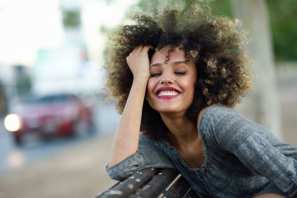 زن جوان سیاه‌پوست با مدل موی افرویی که در پس‌زمینه شهری لبخند می‌زند