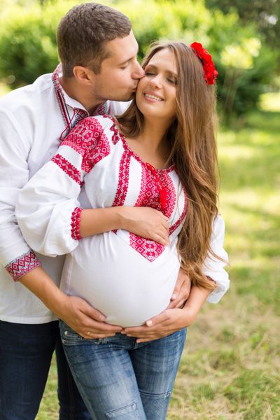 زوج زیبای باردار جوان با لباس ملی اوکراین در حال بوسیدن در پارک پاییز مفهوم سعادت مادر و خانواده