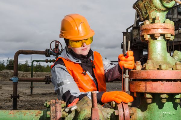 مهندس زن در میدان نفتی در حال تعمیر سر چاه با آچار با کلاه ایمنی نارنجی و لباس کار مفهوم نفت و گاز