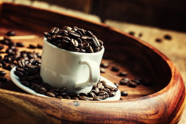 دانه های قهوه در یک فنجان روی سینی تمرکز انتخابی