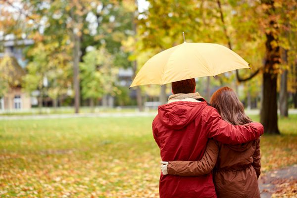 زوج خوشبخت با چتر قدم زدن در پارک پاییزی