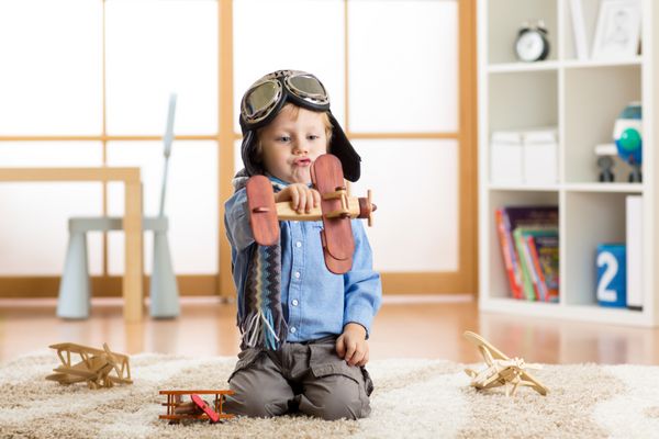 پسر بچه ای که تظاهر به خلبانی می کند بچه بازی با هواپیماهای اسباب بازی در خانه مفهوم سفر و رویا