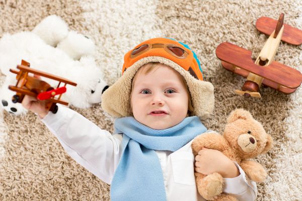 کودک شاد در حال بازی با هواپیمای اسباب بازی پسر بچه ای که روی فرش کرکی دراز کشیده است