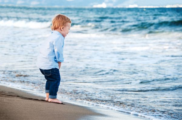 پسر بچه ناز در ساحل دریا را تحسین می کند پاهای برهنه خوشحال