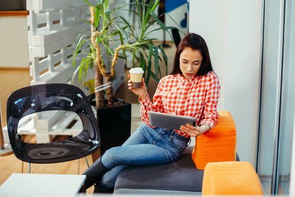 زن جوان در استراحت قهوه با استفاده از تبلت دیجیتال در دفتر