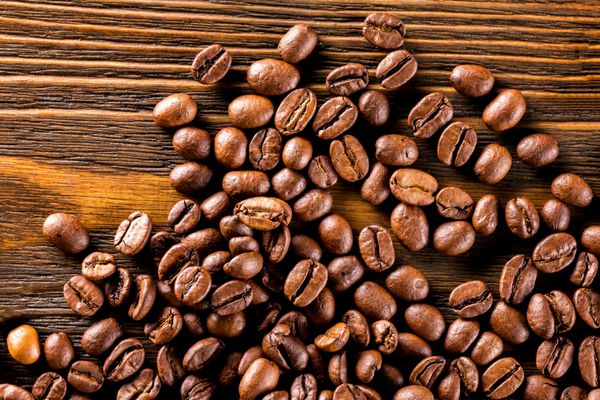 تصویر ماکرو از دانه‌های قهوه برشته شده در پس‌زمینه تخته چوبی بافت‌دار قهوه‌ای