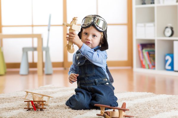 کودک خلبان خلبان با هواپیماهای اسباب بازی چوبی روی زمین در اتاقش بازی می کند