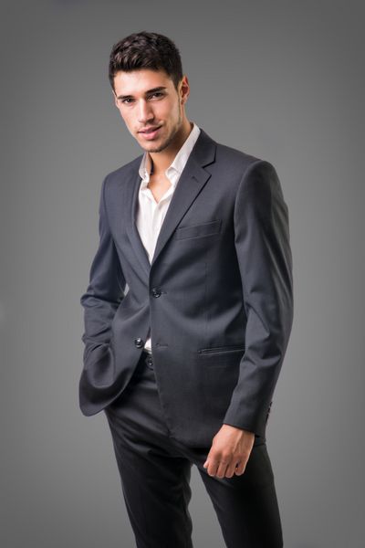 تاجر جوان با اطمینان در مقابل دوربین کت و شلوار تجاری بدون کراوات با پیراهن باز روی گردن در پس زمینه تیره