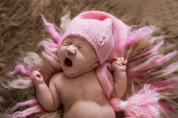 نوزاد شیرین تازه متولد شده با کلاه صورتی خمیازه می کشد و دراز می کشد بیدار می شود