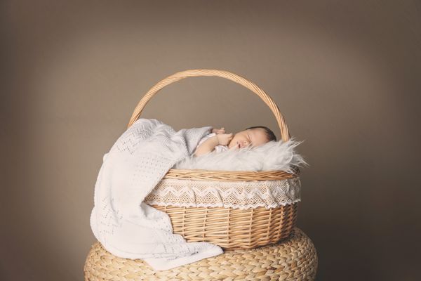 نوزاد کوچولوی ناز در سبد حصیری روی پس زمینه رنگی خوابیده است
