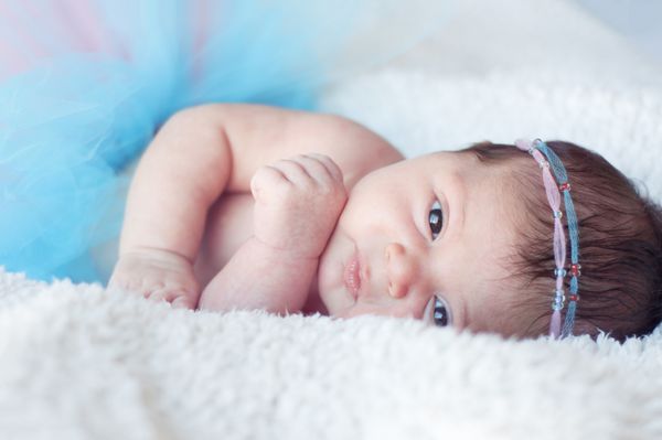 دختر نوزاد تازه متولد شده پرتره یک دختر تازه متولد شده با دامن کرکی و هدبندهای صورتی - آبی با مهره بچه مستقیم نگاه می کند