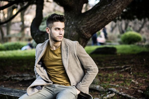 مرد جوان خوش تیپی که در پارک شهر نشسته و در عصر پاییز یا بهار با اعتماد به نفس و آرامش به نظر می رسد
