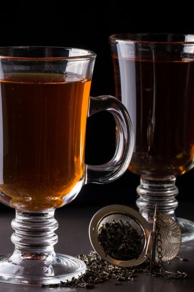 یک لیوان چای با یک صافی روی زمینه تیره