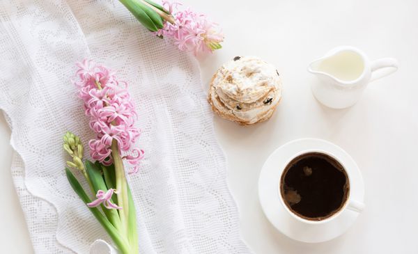 صبحانه عاشقانه صبحگاهی فنجان قهوه کوزه شیر و کیک با دکور سنبل صورتی مفهوم بهار نمای بالا