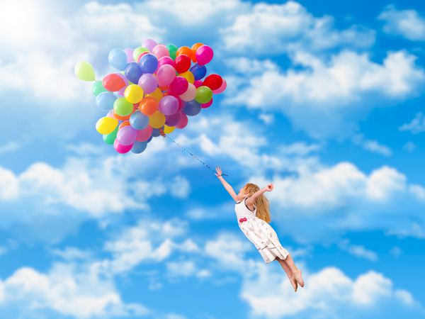 کودک روی بالن ها پرواز می کند آسمان آبی ابر دختر بچه ای با لباس سفید