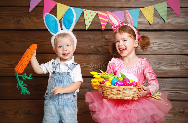 پسر و دختر بچه های شادی که به عنوان خرگوش عید پاک با سبدی از تخم مرغ روی چوب لباس پوشیده اند