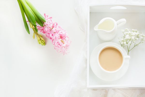صبحانه صبح در بهار با یک فنجان قهوه سیاه با شیر در رنگ های پاستلی دسته گلی از سنبل صورتی تازه در زمینه سفید نمای بالا و فضای کپی