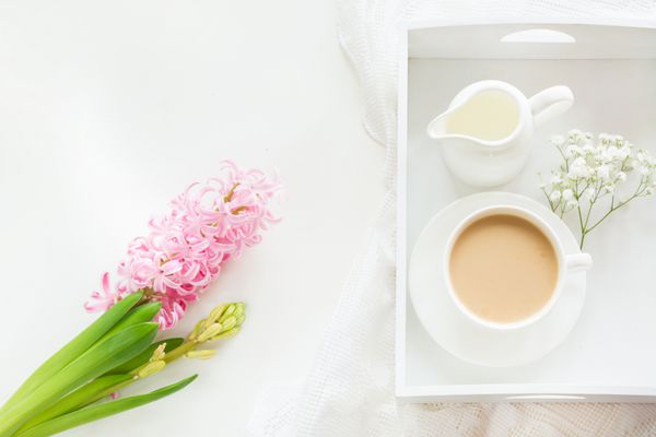 صبحانه صبح در بهار با یک فنجان قهوه سیاه با شیر در رنگ های پاستلی دسته گلی از سنبل صورتی تازه در زمینه سفید نمای بالا و فضای کپی