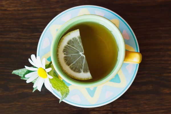 فنجان چای گیاهی با برگ بابونه و نعناع روی زمینه چوبی
