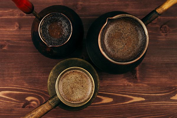 قهوه داغ در ظروف ترکی کهنه با خامه خوشمزه روی پس زمینه تخته چوبی قدیمی قهوه ای نمای بالا سبک روستیک
