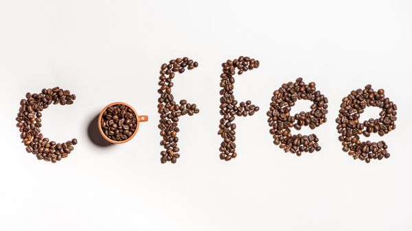 نمای بالای قهوه کلمه ساخته شده از دانه های قهوه در فنجان و روی سفید