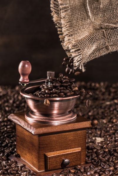 نمای نزدیک آسیاب قهوه با دانه های قهوه معطر روی قهوه ای