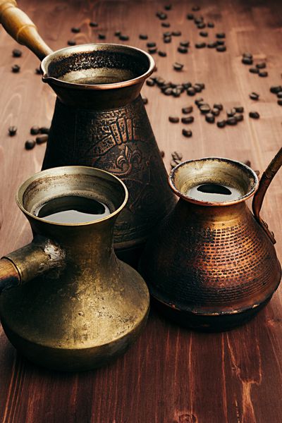 قهوه داغ در قابلمه‌های ترکی عتیقه گروهی با خامه دانه‌های تار روی پس‌زمینه تخته چوبی قدیمی قهوه‌ای عکس عمودی سبک روستیک