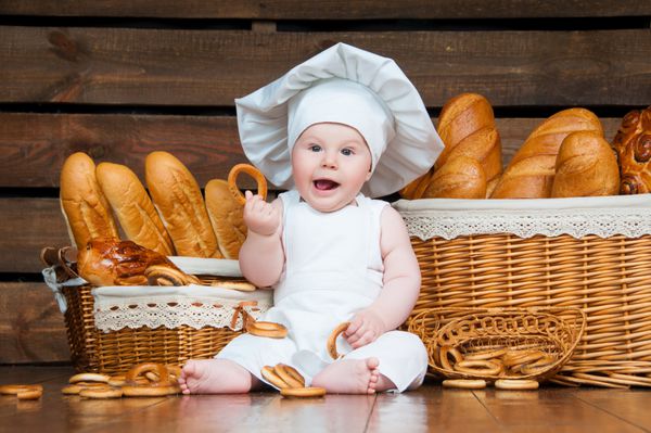 کودک آشپزی در حال خوردن شیرینی روی پس زمینه سبدهایی با رول و نان