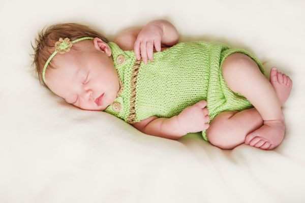 دختر نوزاد تازه متولد شده با کت و شلوار سبز و با تزئین گل کوچک روی سر