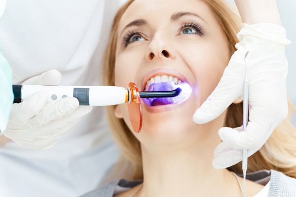 نمای نزدیک از دندانپزشک با استفاده از لامپ UV کیورینگ دندان روی دندان های بیمار