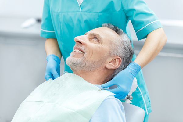 عکس برش خورده بیمار بالغ و دندانپزشک خندان در دستکش های پزشکی