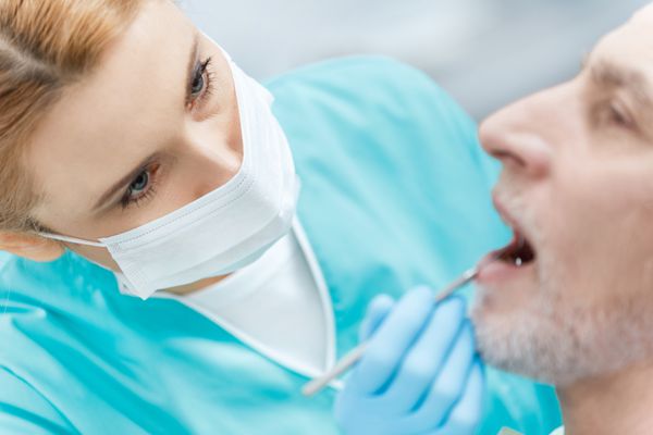 دندانپزشک حرفه ای در ماسک پزشکی بیمار بالغ را در کلینیک درمان می کند