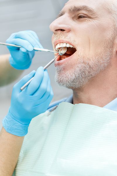 نمای نزدیک از دندانپزشک در حال درمان بیمار بالغ در کلینیک دندانپزشکی