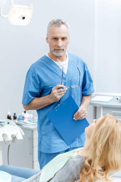 دندانپزشک ارشد با لباس فرم با بیمار در کلینیک دندانپزشکی صحبت می کند
