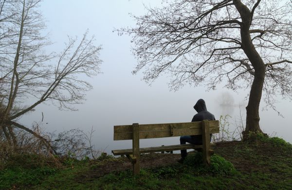 مرد افسرده روی نیمکتی کنار دریاچه نشسته است