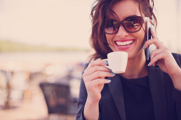زن جوان در کافه قهوه می نوشد و با تلفن همراه صحبت می کرد