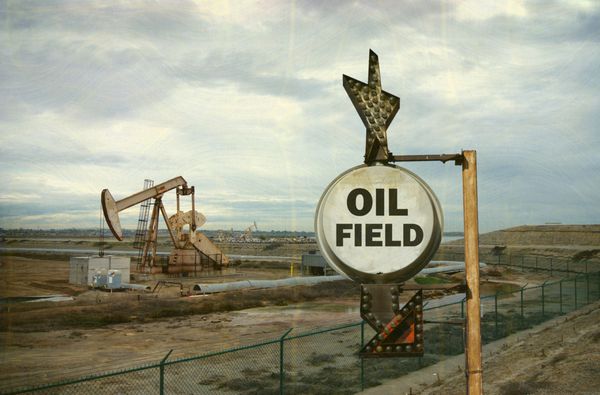عکس قدیمی و فرسوده از تابلوی میدان نفتی با ستون در پس‌زمینه