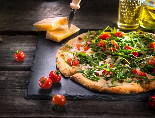 پیتزا کاپرز با آرگولا پنیر ماست و گوجه گیلاسی از نمای نزدیک پیتزای گیاهی خوشمزه خانگی روی میز چوبی غذا