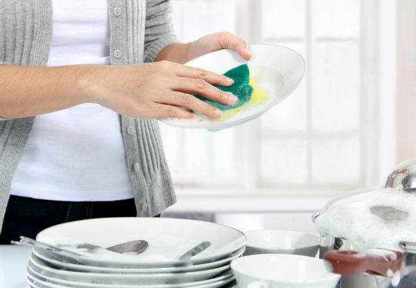 دست های زن در حال شستن ظروف در آشپزخانه از نزدیک