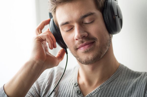 مرد جوان خوش تیپ در حال گوش دادن به موسیقی پسری با هدفون با چشمان بسته در پس زمینه خاکستری