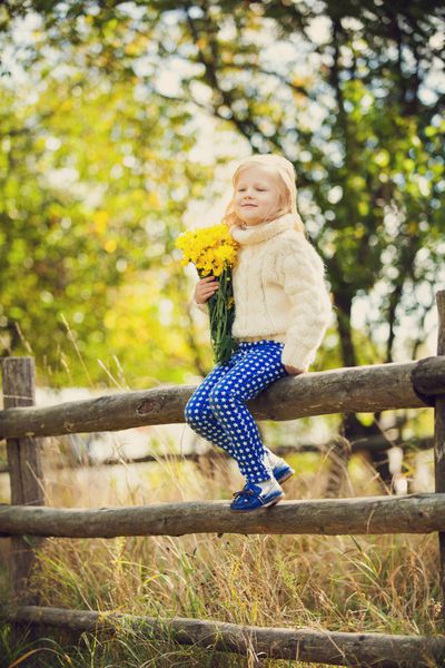 دختر کوچک نشسته روی حصار با دسته گل - دختر شاد