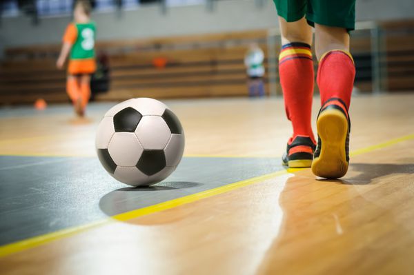 آموزش فوتبال برای کودکان بازیکن جوان فوتبال داخل سالن با یک توپ فوتبال در یک سالن ورزشی پس زمینه ورزشی